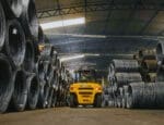 Empilhadeira movimentando bobinas de aço em galpão industrial da Udiaço, referência em corte e dobra industrializado.
