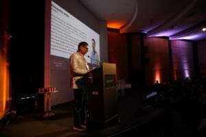 Alexandre Britez, Diretor da Holding GP&D, realiza a mediação do Seminário de Alvenaria Estrutural do C3, discursando no palco com sua apresentação projetada ao fundo.