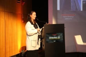 Julia Manoel, Diretora de Projetos da KAZZAS, apresenta palestra no palco do Seminário de Alvenaria Estrutural do C3, ao lado de púlpito com a identidade visual do evento.