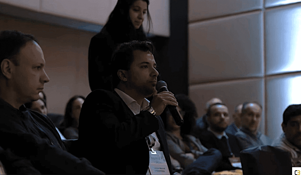 Marcos Barral participa do Painel de Debates no Seminário de Alvenaria Estrutural, segurando microfone e interagindo com o público em auditório lotado.