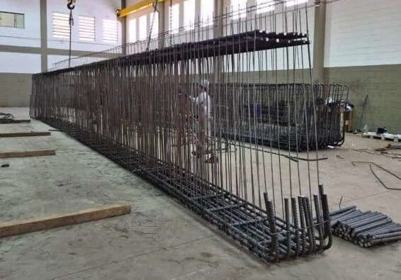 Estrutura de viga pré-armada sendo movimentada por ponte rolante em ambiente industrial da Aços Urano, destacando tecnologia e precisão na fabricação.