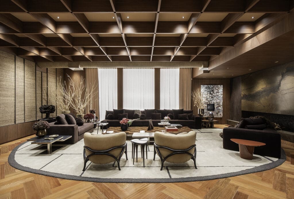 Sala de estar sofisticada com mobiliário SCA, tons amadeirados, forro treliçado em madeira e decoração contemporânea, projeto de Denise Barretto para a Mostra Artefacto 2026.