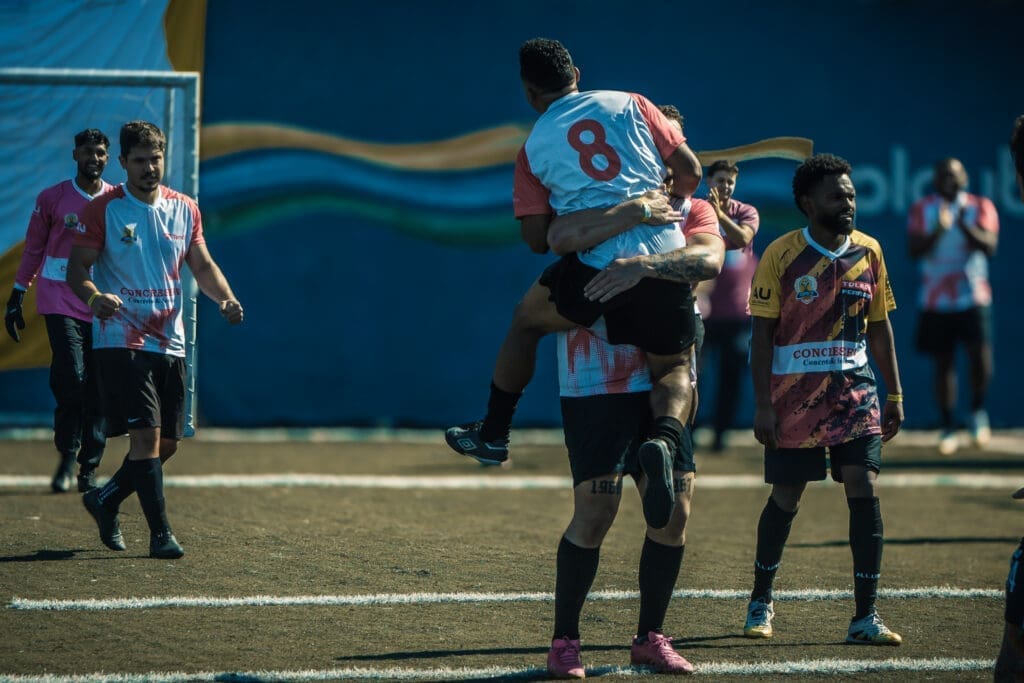 Jogadores comemoram gol durante partida do Torneio Integração da Copa C3 2026, com atleta sendo erguido pelo companheiro em campo, expressando alegria e união.