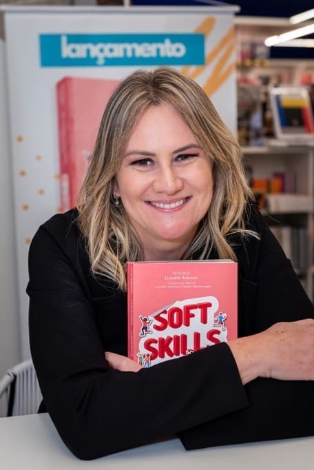 Lucedile Antunes sorrindo, segurando o livro “Soft Skills” durante evento de lançamento, em ambiente de livraria.