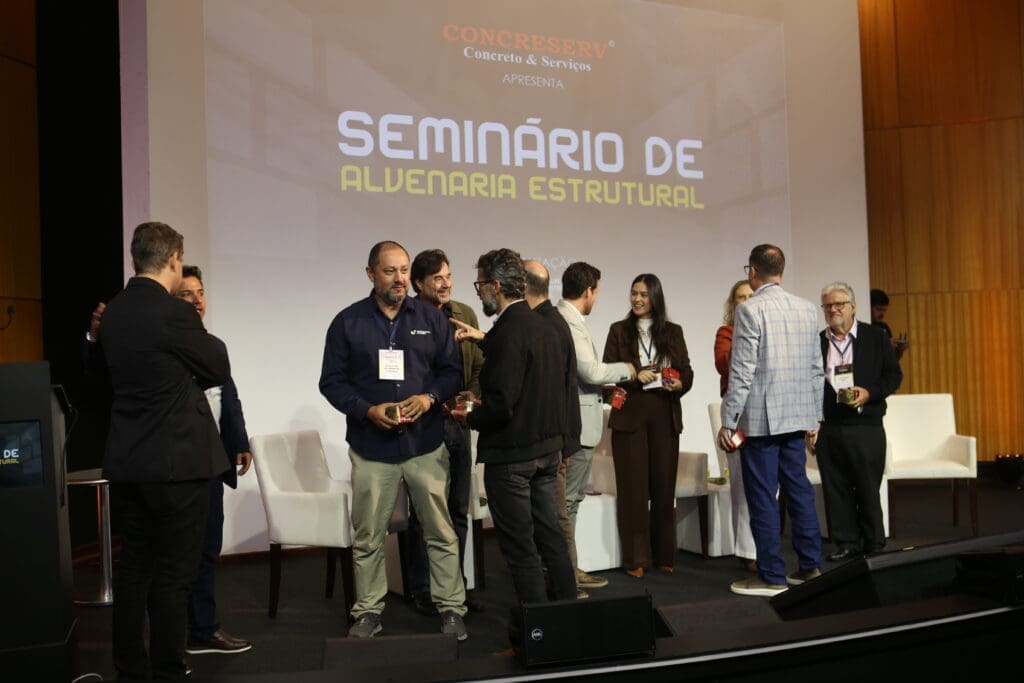Palestrantes e organizadores interagem no palco durante o Seminário de Alvenaria Estrutural, promovido pela Concreserv, com o telão do evento ao fundo.
