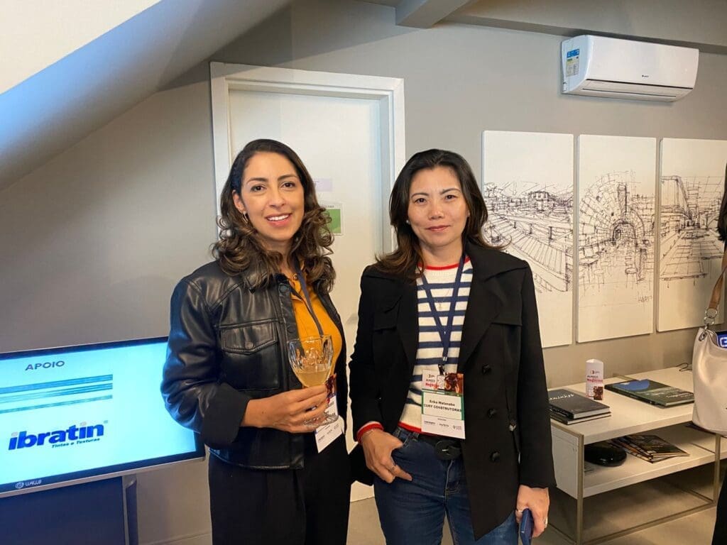 Camila Basso e Erika Watanabe, da Cury Construtora, posam sorridentes durante o 65° Almoço de Negócios do C3, em ambiente moderno e decorado.