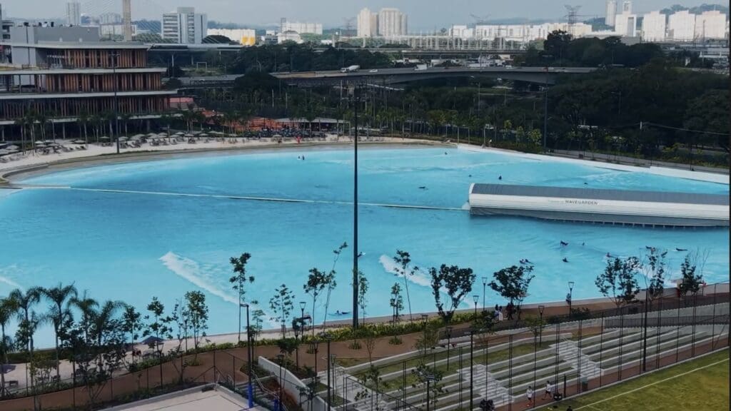 Vista aérea da piscina de ondas do Beyond The Club São Paulo, com surfistas aproveitando as ondas artificiais, áreas de lazer ao redor e o cenário urbano da cidade ao fundo.
