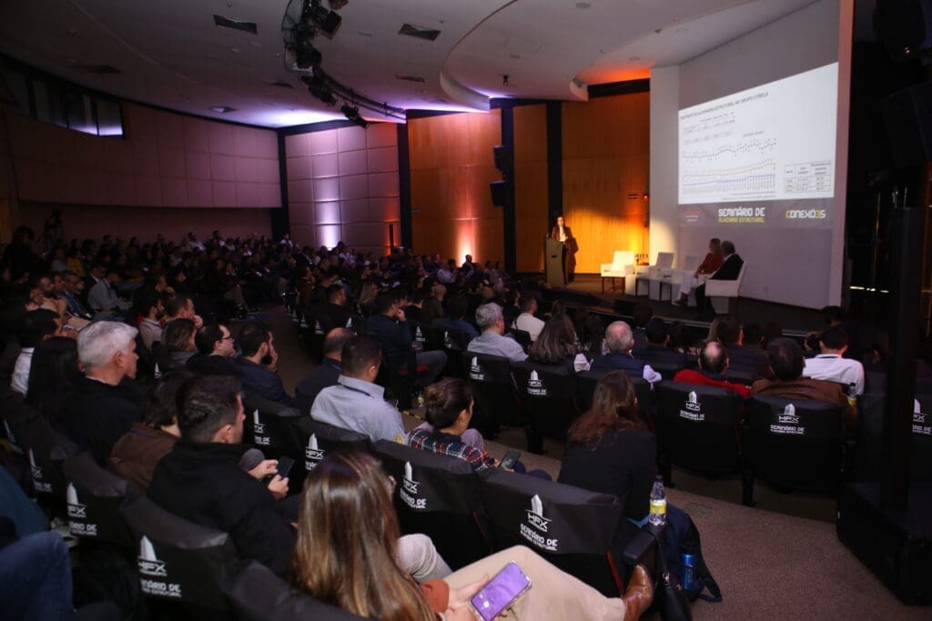 Auditório lotado acompanha palestra técnica durante o Seminário de Alvenaria Estrutural, com apresentação de gráficos projetados no telão e painel de especialistas no palco.