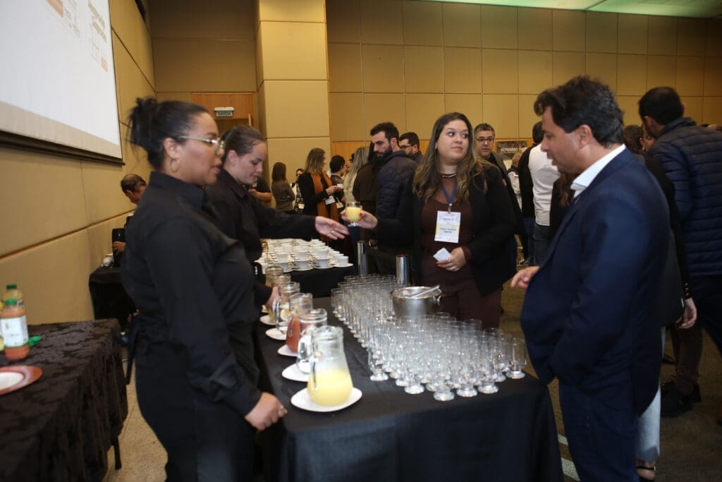 Marcos Barral, da Oterprem, interage com participantes e equipe de serviço durante o coffee break do Seminário de Alvenaria Estrutural, promovendo networking no evento.