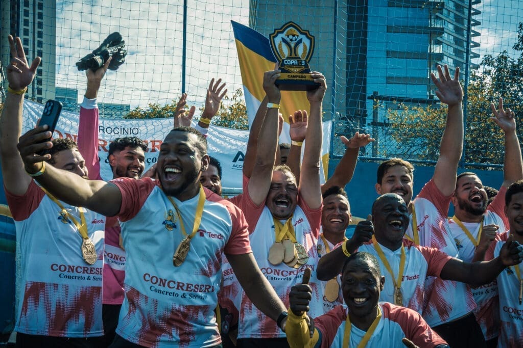Jogadores da equipe Tenda comemoram a conquista do título do Torneio Integração da Copa C3 2026, erguendo o troféu de campeão e exibindo medalhas, com expressões de alegria e união em campo.