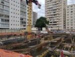 Canteiro de obras com montagem de vigas estruturais pré-armadas em área urbana, destacando a atuação da Aços Urano em projeto de alta complexidade.
