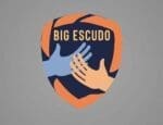 Logo do programa Big Escudo, com duas mãos estilizadas, uma azul e outra bege, se tocando dentro de um escudo laranja e azul, simbolizando proteção e união na luta contra a exploração infantil.