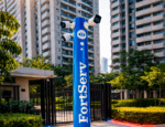 Totem de segurança FortServ com câmeras de vigilância instaladas na entrada de um condomínio residencial moderno, cercado por prédios altos e áreas verdes.