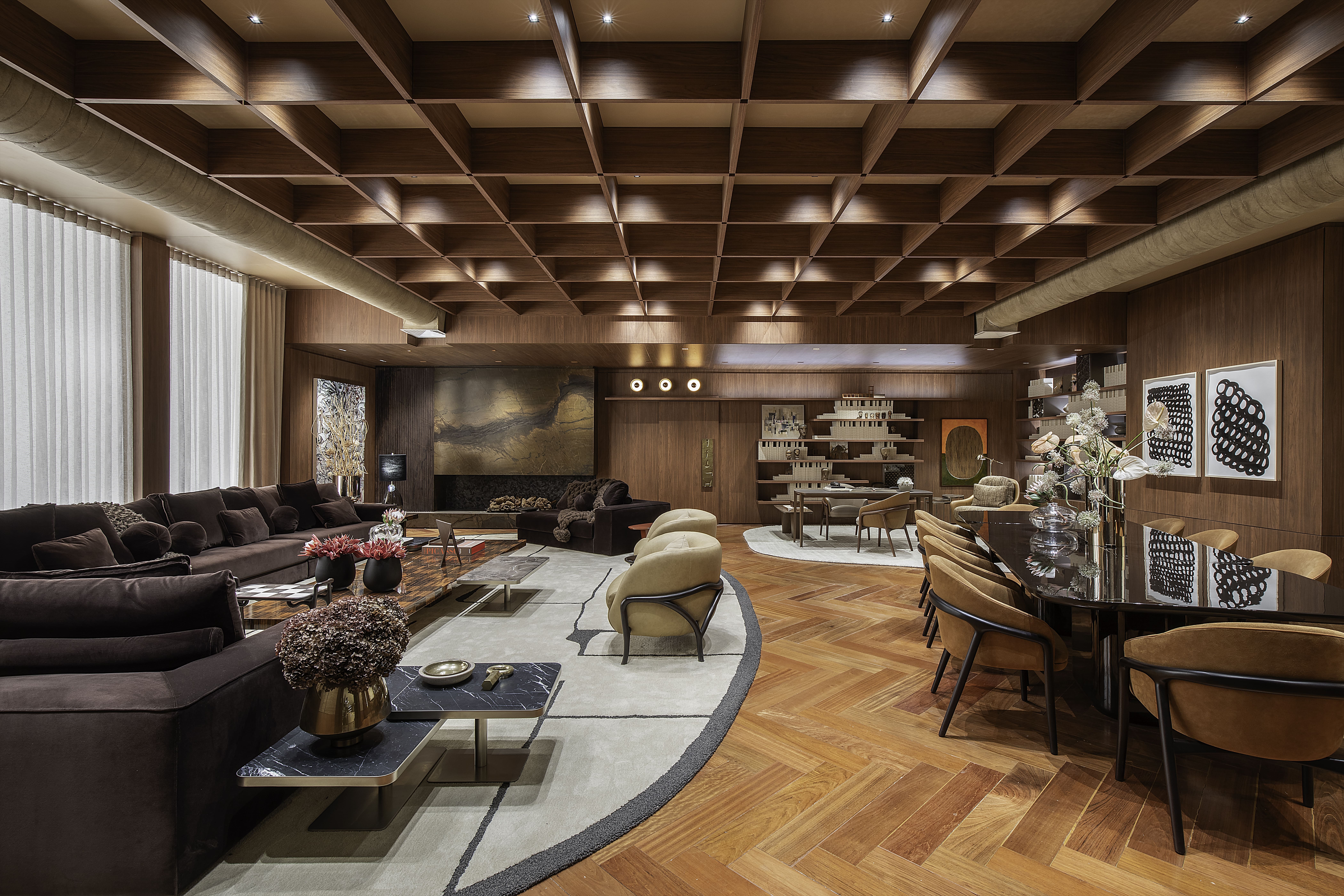 Ambiente sofisticado com sala de estar, jantar e biblioteca integrados, mobiliário sob medida SCA, tons amadeirados e forro treliçado, projeto de Denise Barretto para a Mostra Artefacto 2026.