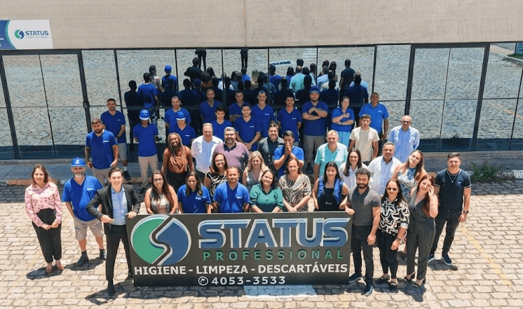 Equipe da Status Pro reunida em frente à sede da empresa, segurando placa com o logotipo e os serviços de higiene, limpeza e descartáveis.