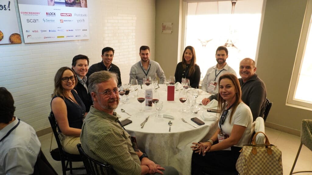 Grupo de profissionais da construção civil reunidos ao redor de uma mesa redonda durante o 66° Almoço de Negócios do C3, em ambiente elegante e iluminado, com crachás de identificação e materiais institucionais ao fundo.