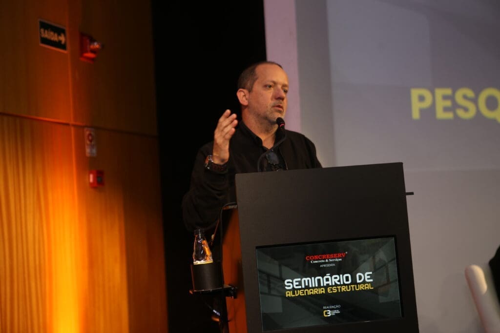 Rodolfo Zagallo, CEO do C3 - O Clube da Construção Civil, discursa no palco durante o Seminário de Alvenaria Estrutural, ao lado de um púlpito com a identidade visual do evento.