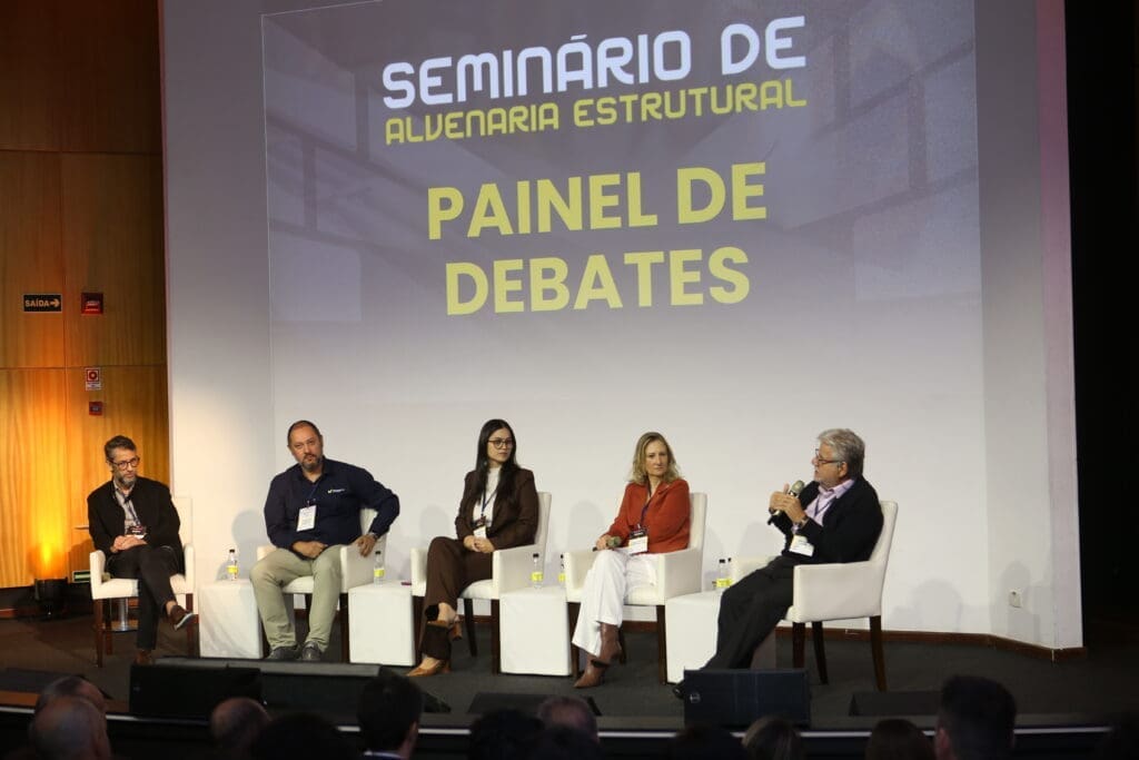 Painel de especialistas debate tendências e desafios da alvenaria estrutural durante o Seminário de Alvenaria Estrutural do C3, com cinco profissionais sentados no palco do auditório.