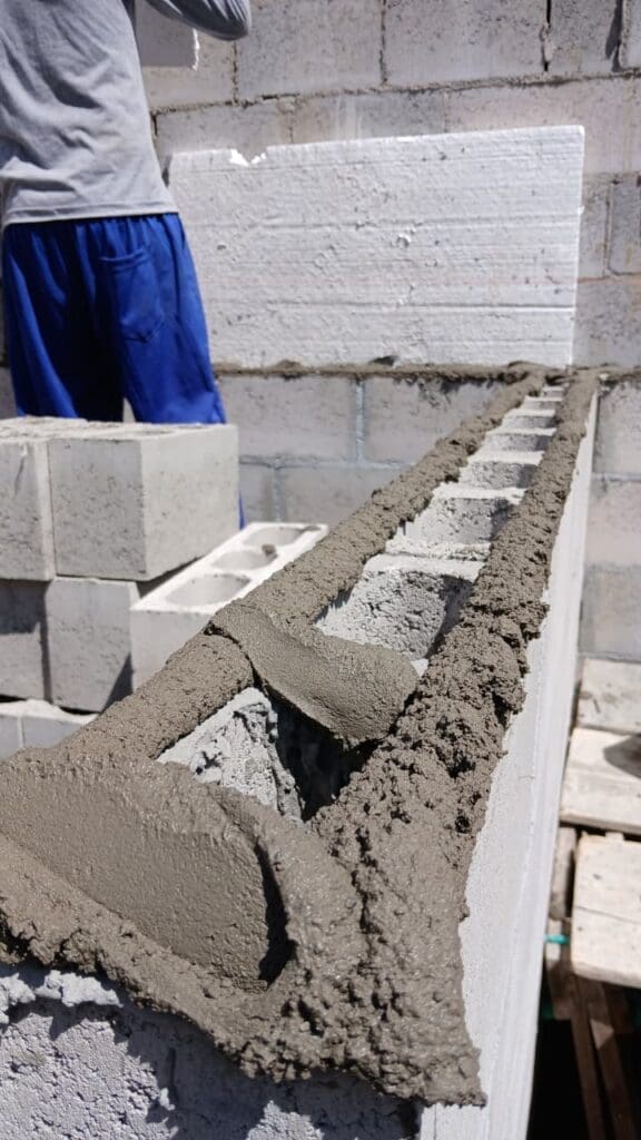 Aplicação de argamassa estrutural sobre blocos de concreto em parede de alvenaria, durante obra de construção civil.