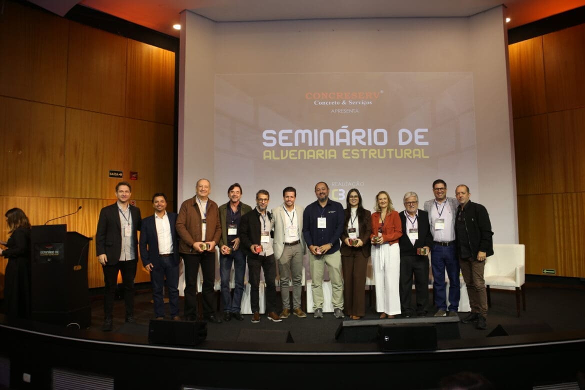 Grupo de palestrantes e painelistas do Seminário de Alvenaria Estrutural do C3 - O Clube da Construção Civil, posando juntos no palco do auditório, com o telão ao fundo exibindo o nome do evento.