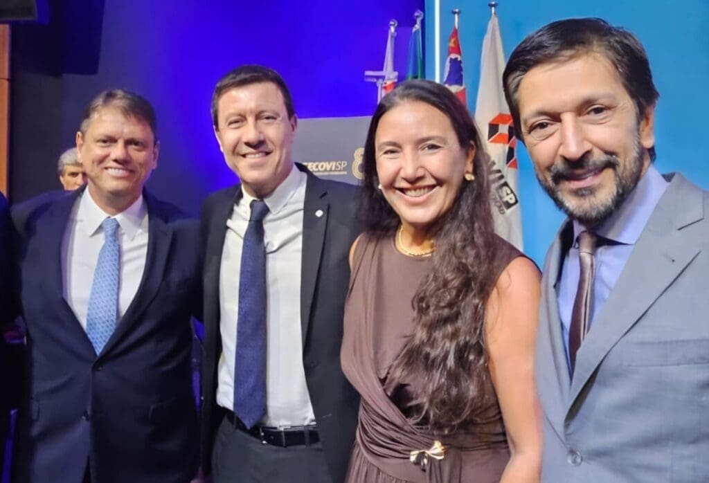 Quatro líderes do setor público e privado posam sorrindo durante a cerimônia de posse da diretoria do Secovi-SP, com bandeiras ao fundo e iluminação azul.